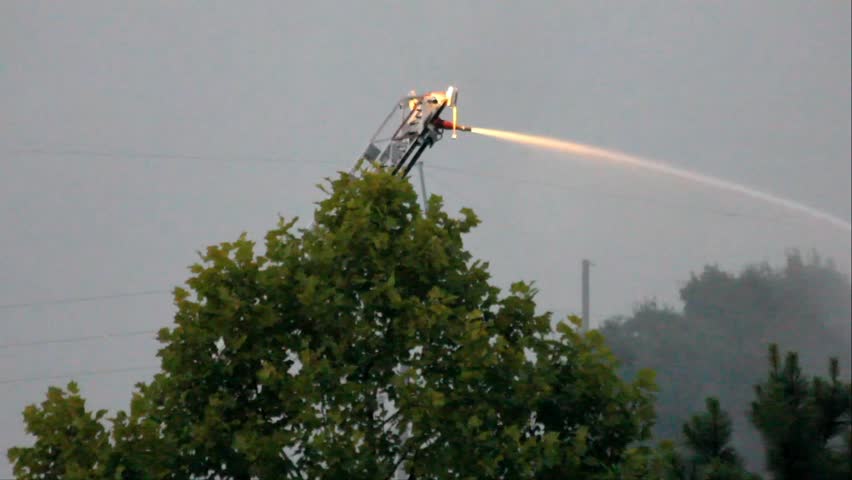 Firefighter Water Cannon On Tall Ladder At Dusk At Long Range In Operation