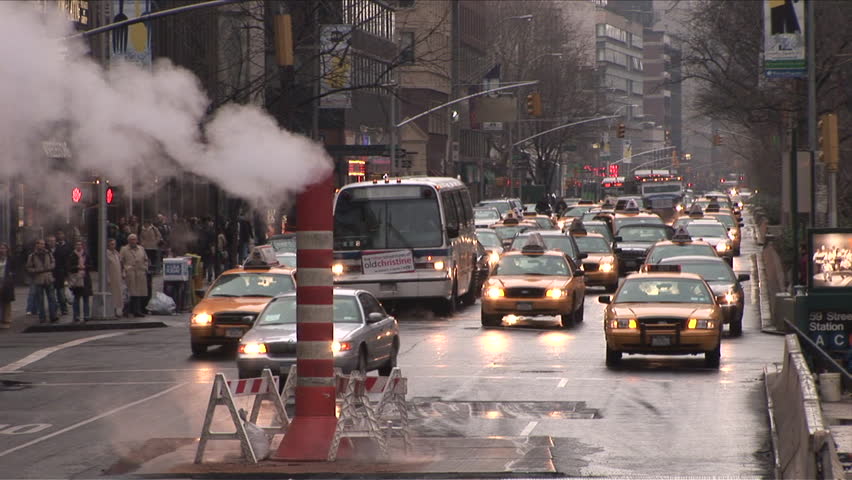 New York, NY - CIRCA March 2006: Rush hour traffic drives past a smokestack spewing steam on a busy avenue