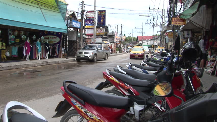 Ko Samui, Thailand - CIRCA December, 2006: A shot of traffic going down the street with a line of parked scooters in the foreground