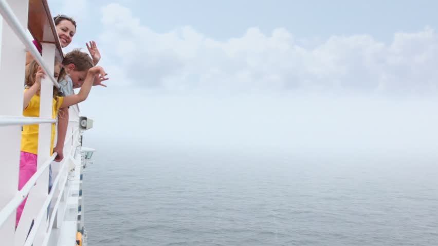 Mother with her kids stand on deck near fence and wave hands during cruise