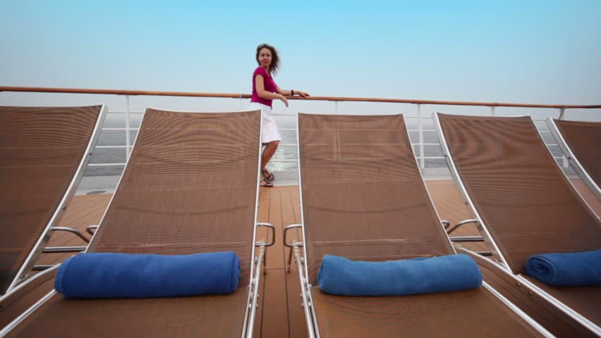 Woman stands on deck near fence behind few deckchairs during cruise