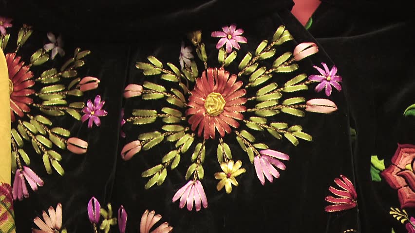 Close Up Of Intricate Stitching; Zoom Out to See Large Display of Handcrafted Clothing Being Sold In A Mexican Marketplace