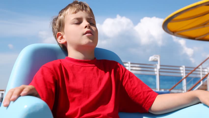 Boy sleeps in chaise lounge on ship deck in sunny weather