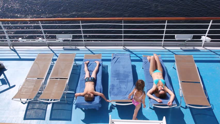 Mother, daughter and son sunbathe in chaise lounges on board ship