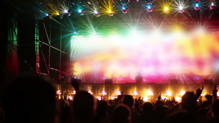 atmospheric slow motion shot of the crowd looking towards the stage at a dance music festival. the crowd is in shadow