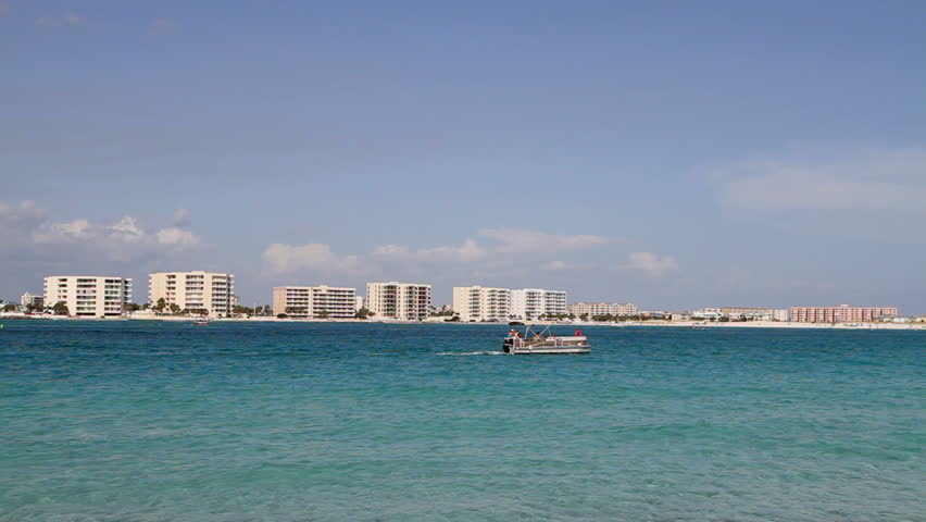 Pontoon boat powers out Destin Pass along the blue-green waterway with condominiums on the far beach of Destin, Florida, USA.