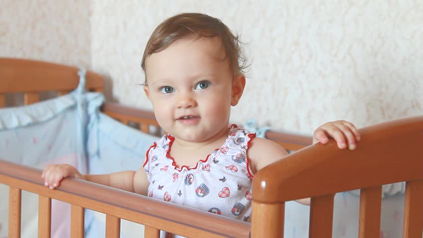 Beautiful happy smiling baby girl standing in bed and looking with interest