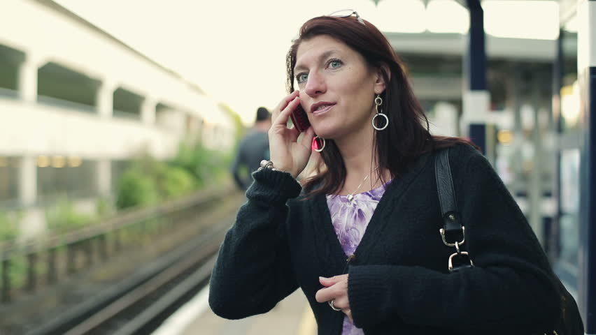 Woman talking on cellphone on train station, steadicam shot
