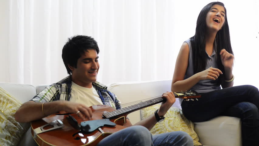 Pan shot of a man playing a guitar for his sister