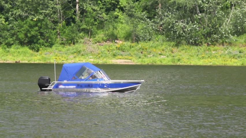 Man sits in cabin of small motor boat and float near coastline with plants