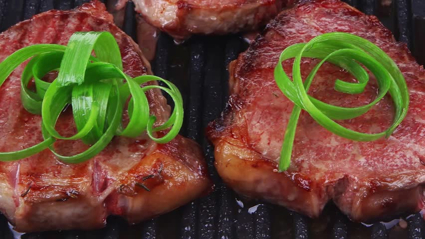 fresh grilled bloody beef steaks on black grill plate with green leaves isolated on white background