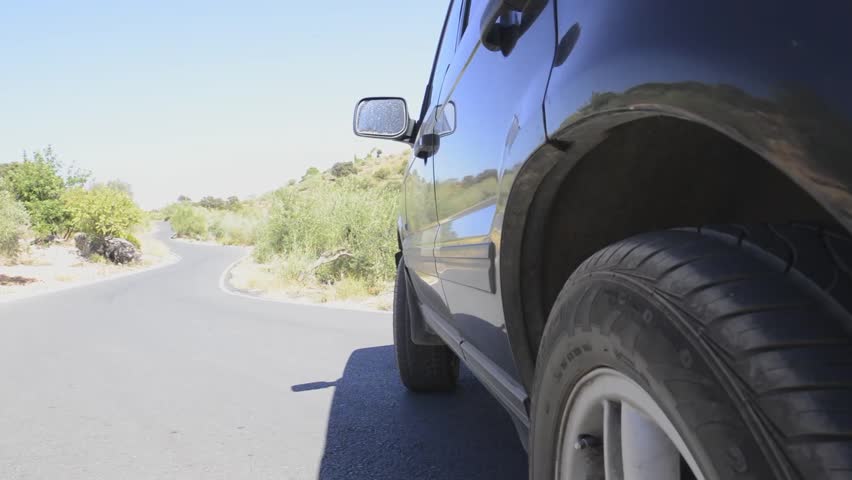 Large four by four drives over a winding road onto a dirt road at high speed.