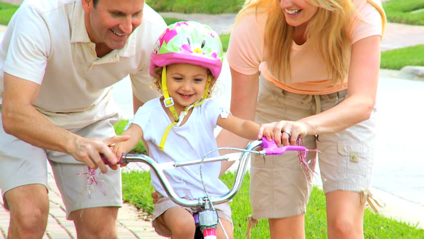 Young parents supporting toddler daughter wearing safety helmet on bicycle