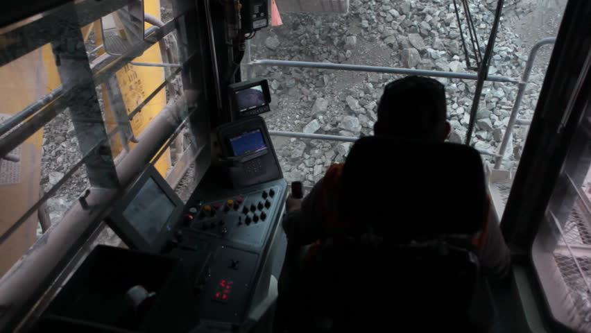 An excavator scoops up a huge bucket of dirt and ore and is about to empty it into the rear tray of the haulage truck. 