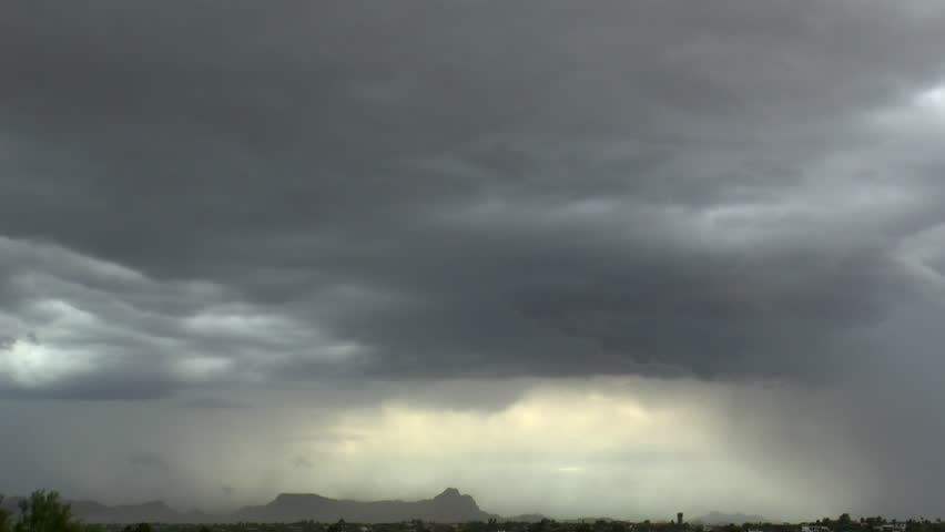 Amazing, unique stormy weather time lapse featuring sandstorm, lightning strike, swirling, fast-moving clouds, strong winds, sweeping rain shafts dumping monsoon rains on  mountainous landscape.  