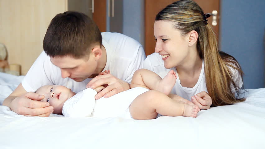 Happy family: father, mother and baby playful in the bedroom