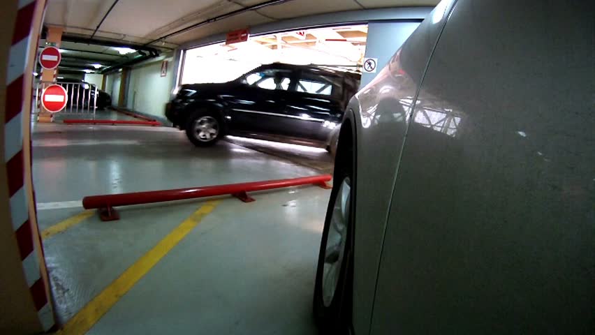Gray car leaves underground garage in which there are other cars