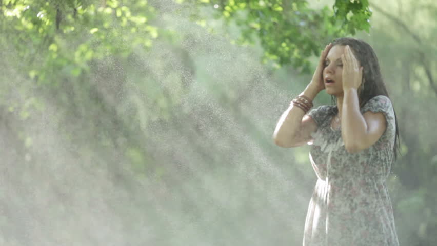 A beautiful girl in a park begins to bustle under the streams of water dances. Spins and is glad