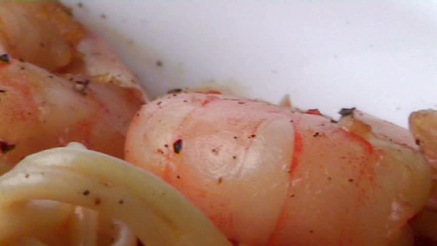Spaghetti and prawns in a cream sauce, garnished with herbs. Served on a deep white, round bowl with wide rim sprinkled with ground pepper. macro close-up, rotating subject