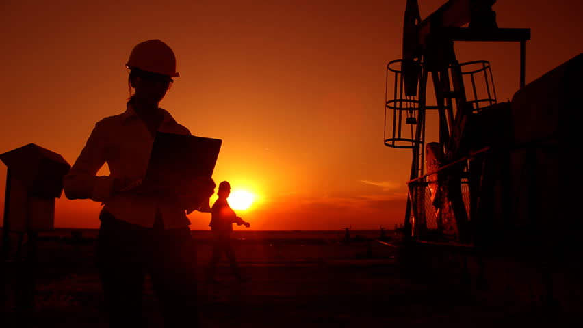 Oil pump jack and two oil workers in a field at sunset