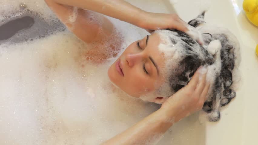 Relaxed woman lying in bubble filled bath washing her hair.