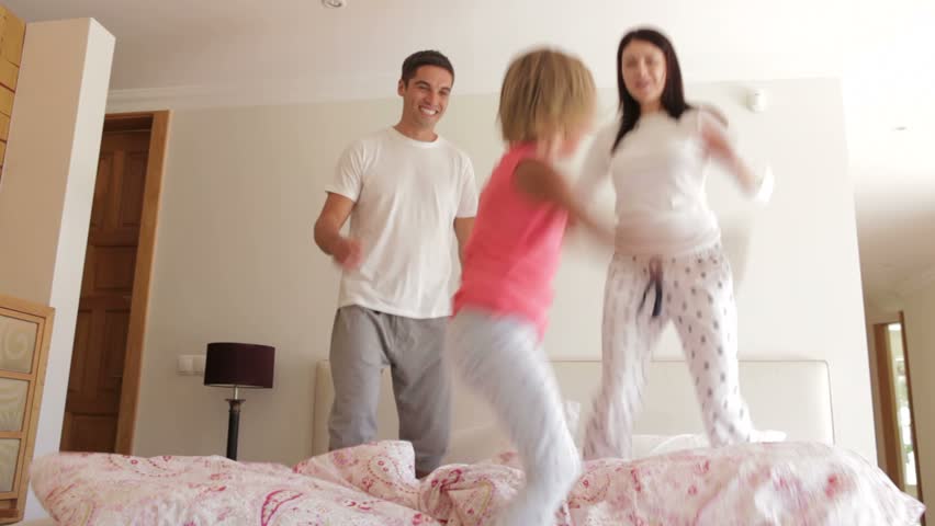 Young girl bounces excitedly on bed with parents.