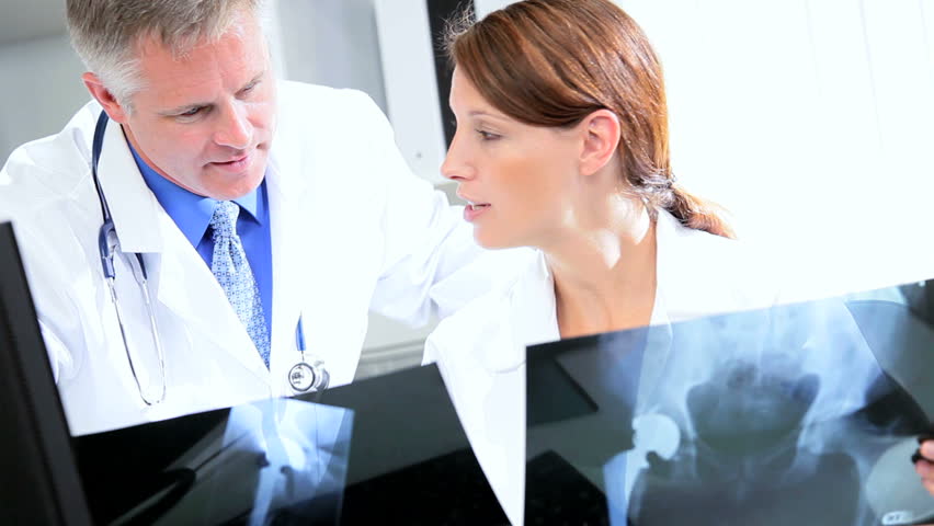 Male female hospital doctors examining patient x-ray results with office computer