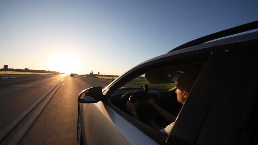 left side of silvery car going toward declining sun with driver at wheel