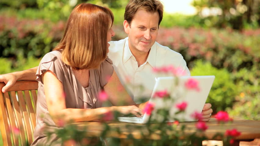 Attractive couple using wireless laptop outdoors garden table