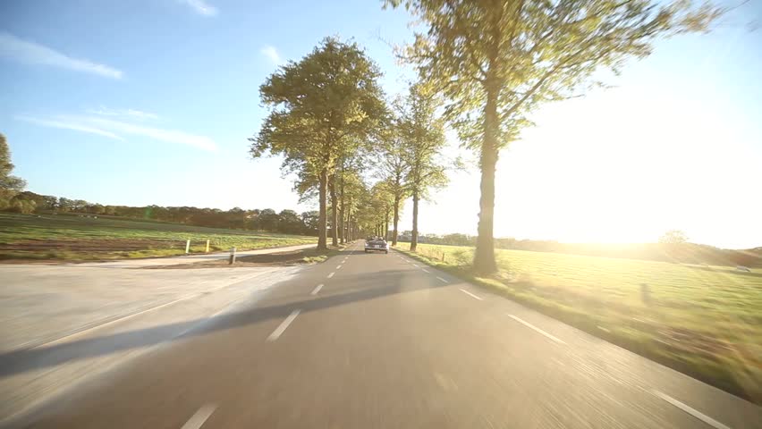 video footage of a on-board camera on a car driving on a country road in the sunset
