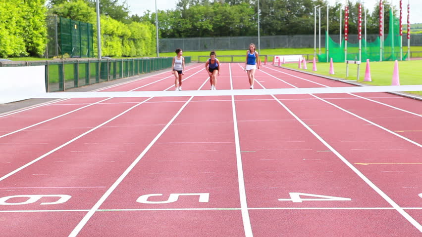 Three woman running on a track and crossing finish line in stadium