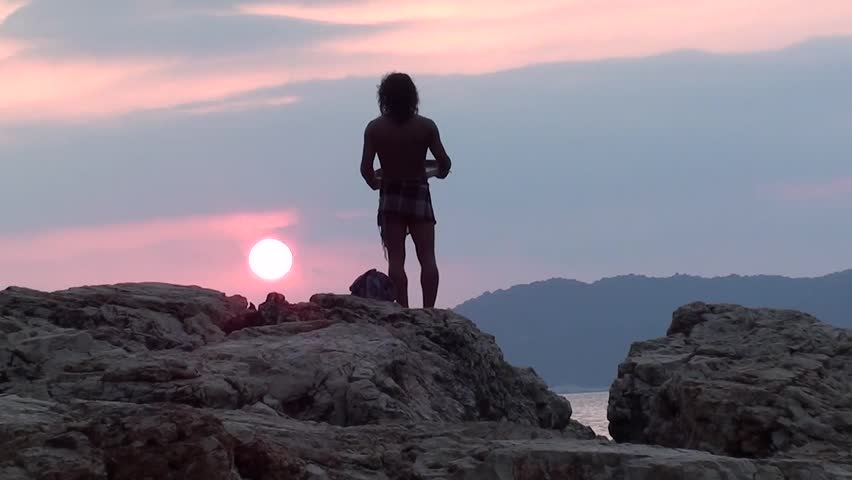Man with tambourine praying on rock to the declining sun