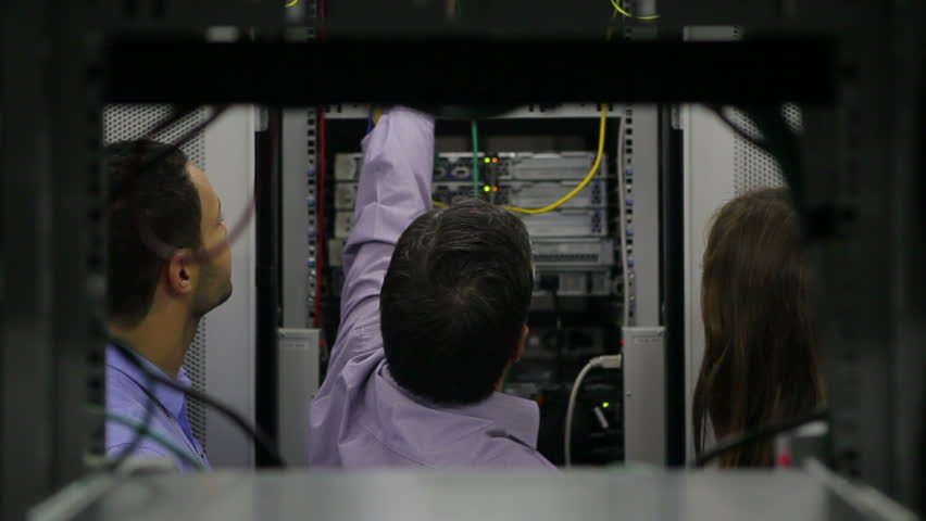 Two persons watching man while fixing wires in hallway of data center
