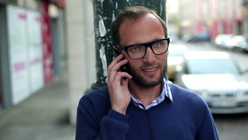 Young man standing on the street and talking on cellphone, stabilized shot
