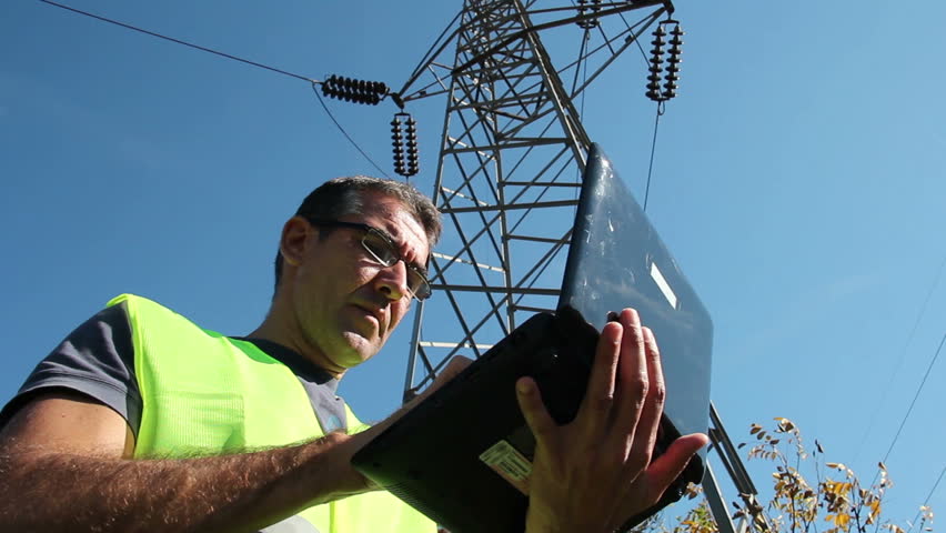 Power Company Worker with Laptop.
Typing on a keypad of laptop under the electric tower.