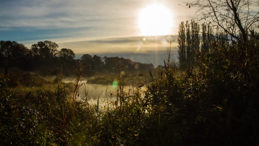 Time Lapse of a Foggy Morning at a Lake. Fog slowly moving on the surface of the lake while the sun light shinning through the fog