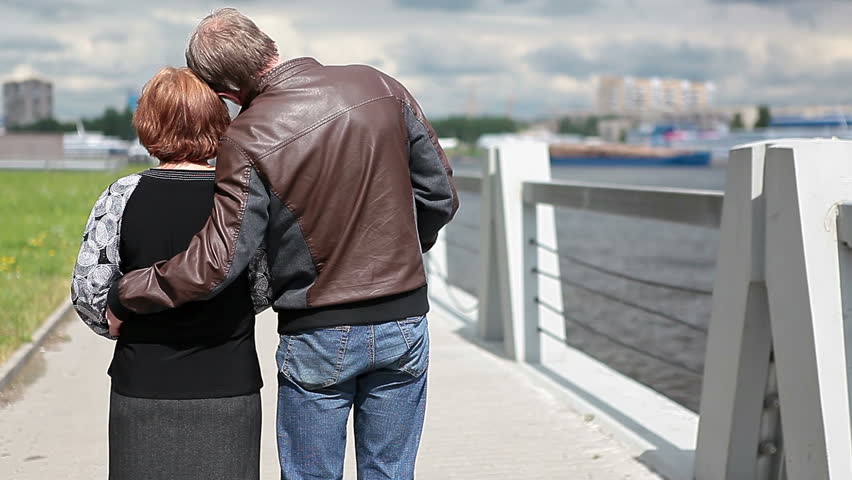 Elderly husband and wife are on the river bank. Turning back and smiling. The Neva River Embankment, St. Petersburg