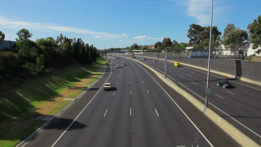 Video of vehicle, car and truck traffic driving away from view from overpass. High speed multiple lane freeway highway. Melbourne Australia.