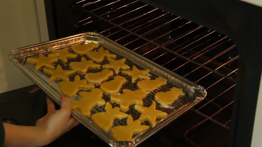 Baking Sugar Cookies 16. Preparing, mixing, baking and decorating Christmas sugar cookies. Putting the prepared cookies on the cookie sheet into a preheated oven.