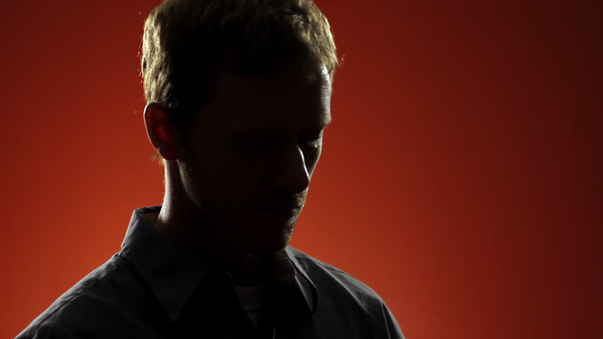 Backlit man with a headache takes a pill with water and then rubs his forehead