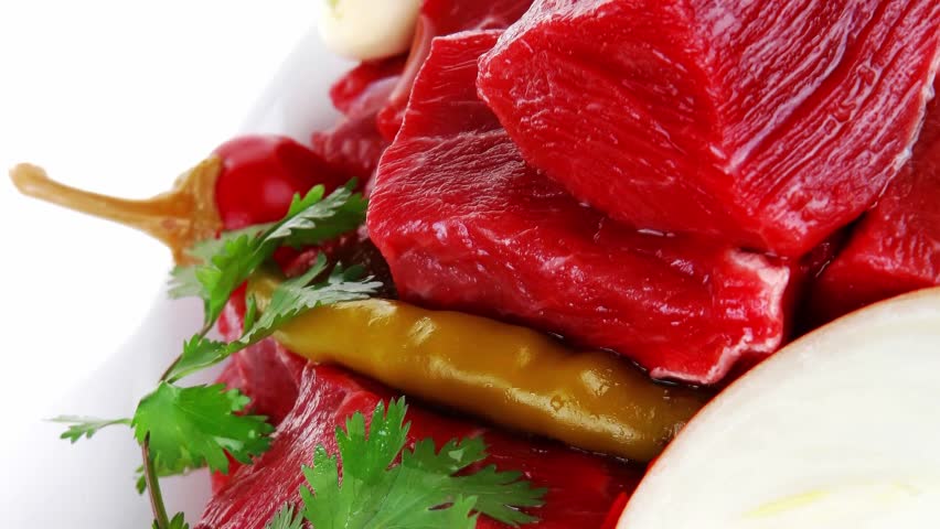 fresh uncooked beef meat slices over white bowls ready to prepare with red peppers and greenery isolated over white background