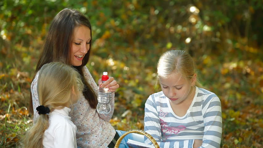 Young mother and two daughters enjoying autumn day at picnic in the park, children drinking water