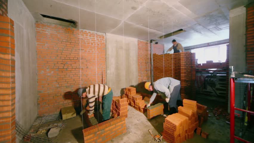 Few workers build brick walls in room at construction site