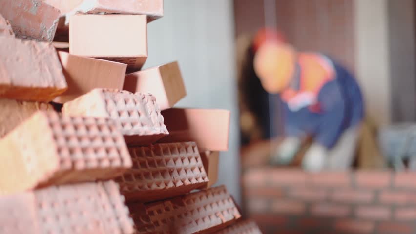 Pile of bricks at background of few workers build wall unfocused