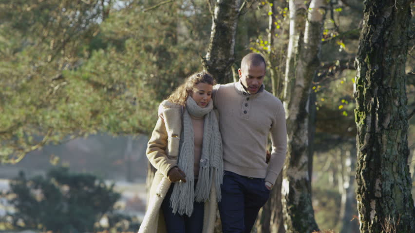 A young couple in love stroll together through a forest in the early morning sunlight. In slow motion.