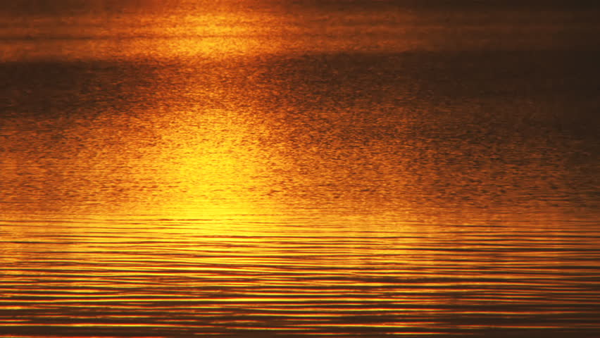 Resplendent sunset reflected off a lake's varied and soothingly patterned surface in the late evening in midsummer Alaska.
