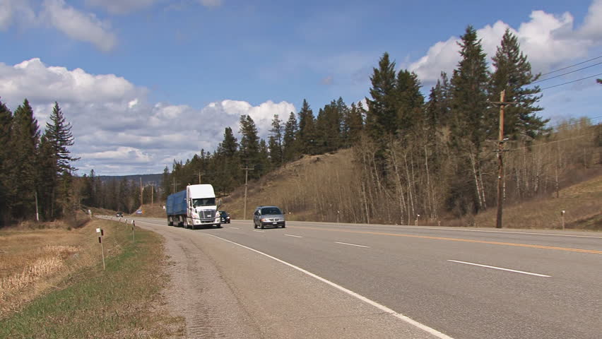 BRITISH COLUMBIA, CANADA - CIRCA 2012: Two tractor-trailer trucks pass by on the Alcan Highway in British Columbia, Canada in the afternoon of a splendid day with puffy cumulus clouds