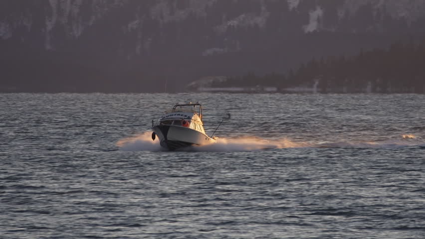 HOMER, AK - CIRCA 2011: A small cabin cruiser fishing boat blasting its way through small waves as the sun sets.
