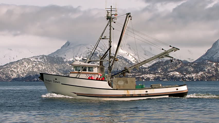 HOMER, AK - CIRCA 2012: An Alaskan trawler returns to port just off the Homer Spit, with the resplendent Kenai Mountains looming in snow-covered glory beyond the azure waves of Kachemak Bay.