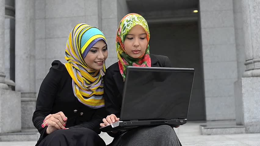 Two young pretty Asian muslim business woman in head scarf with laptop 
